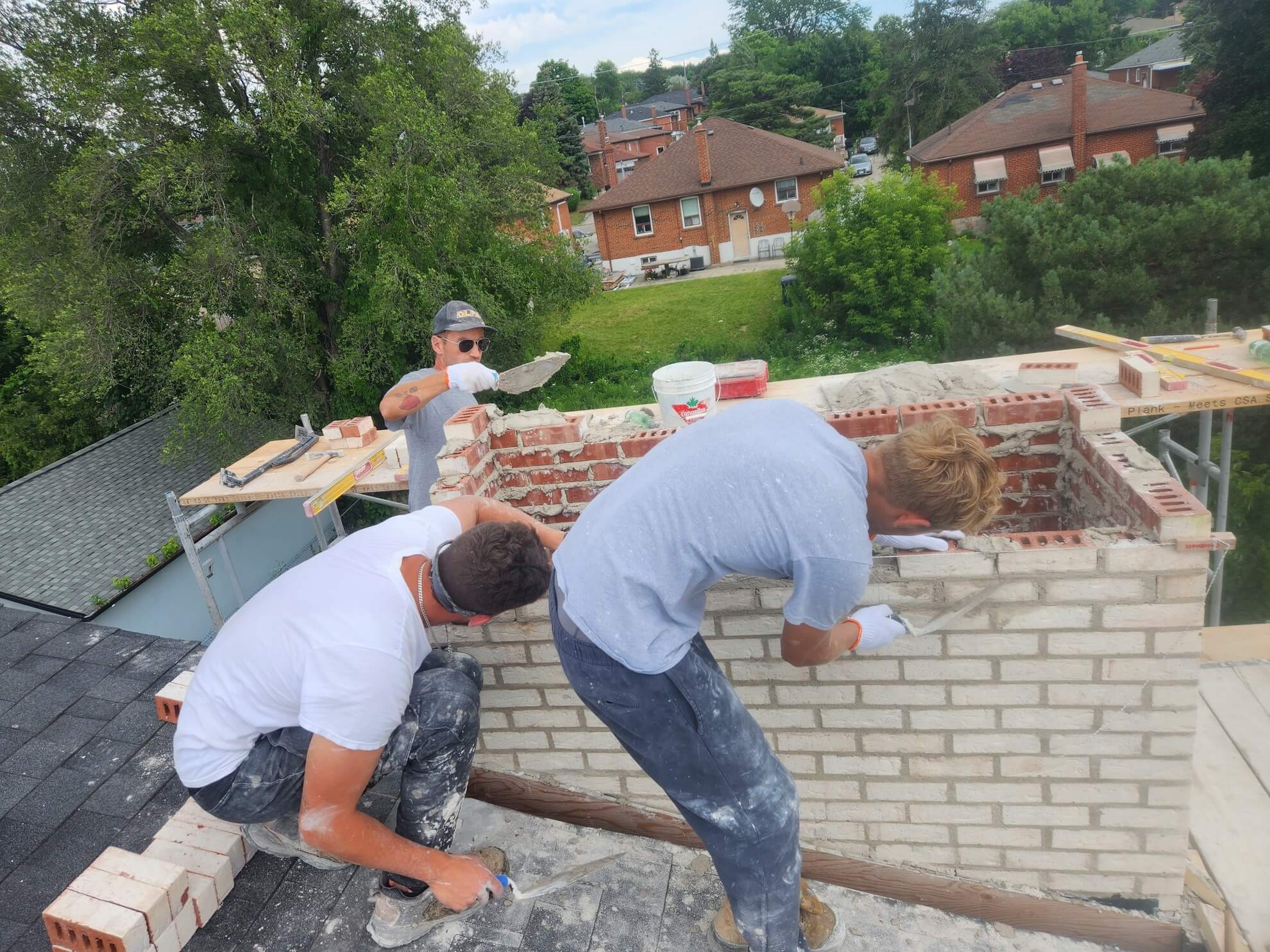 Two masons rebuilding a brick chimney on a residential roof